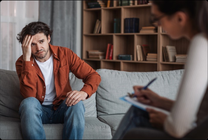 a man sitting on a couch while holding his head listening to his therapist