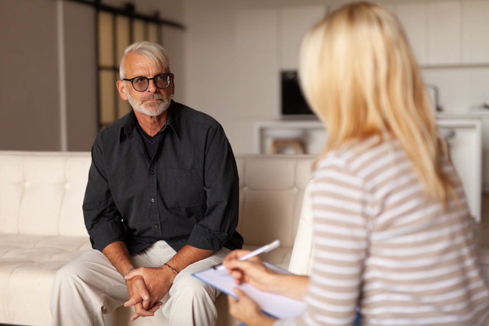 a man wearing glasses sitting on a coach attending individual therapy