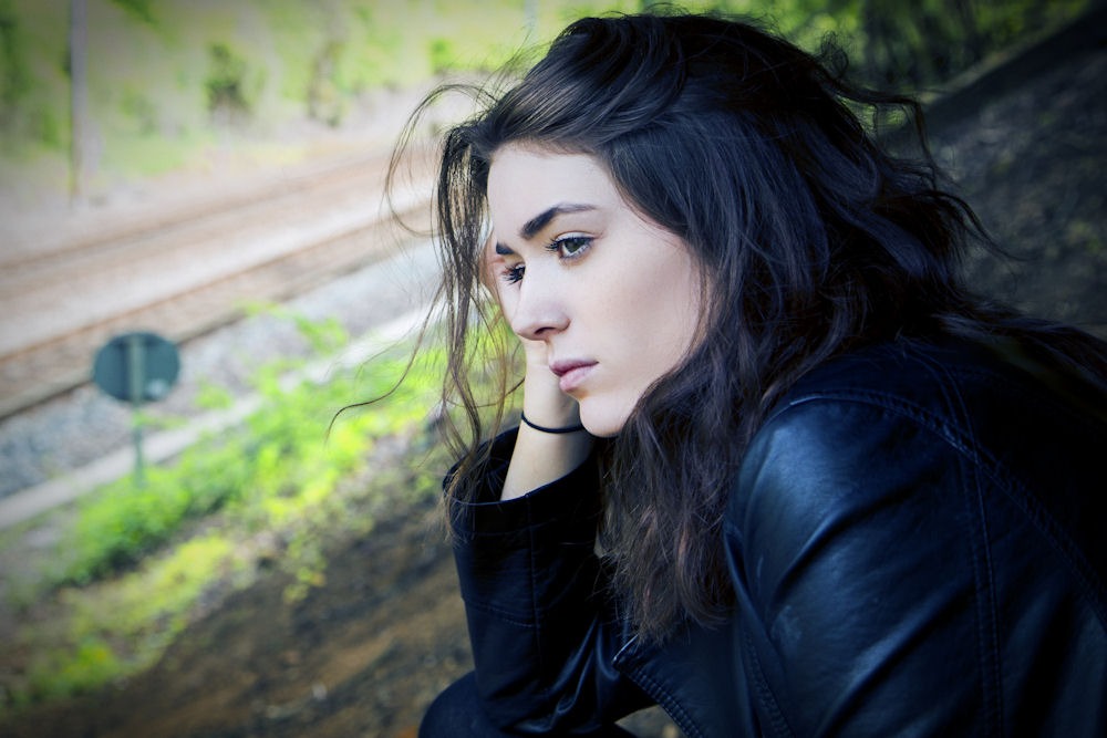 A woman sits on a bench, her head bowed, conveying a sense of contemplation or sadness in a serene environment.