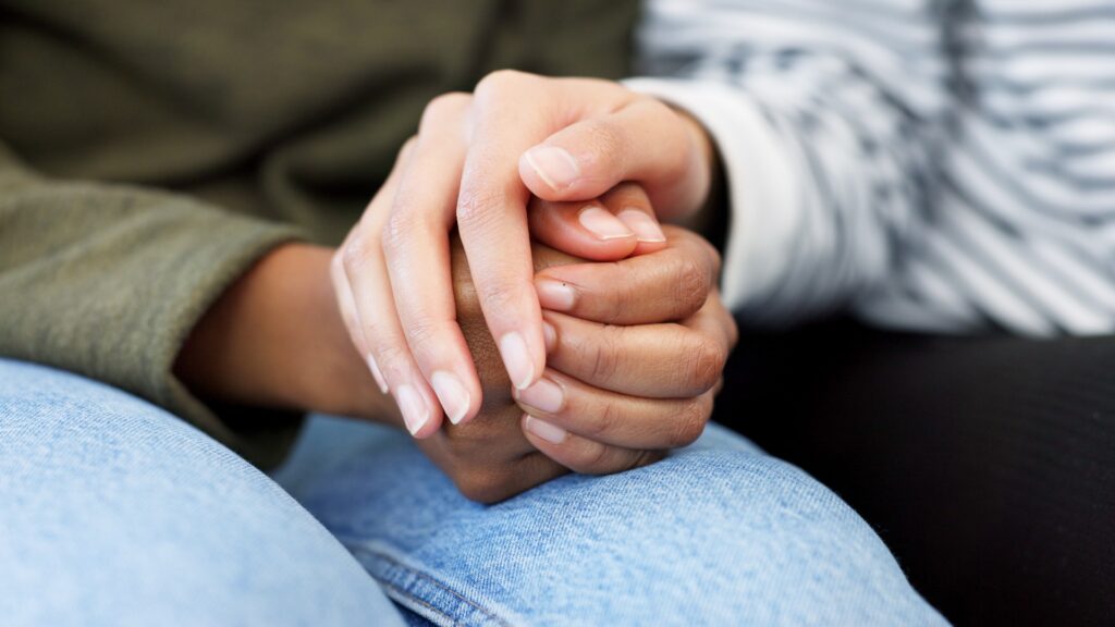 Two individuals holding hands, their palms resting on top of each other in a gesture of connection